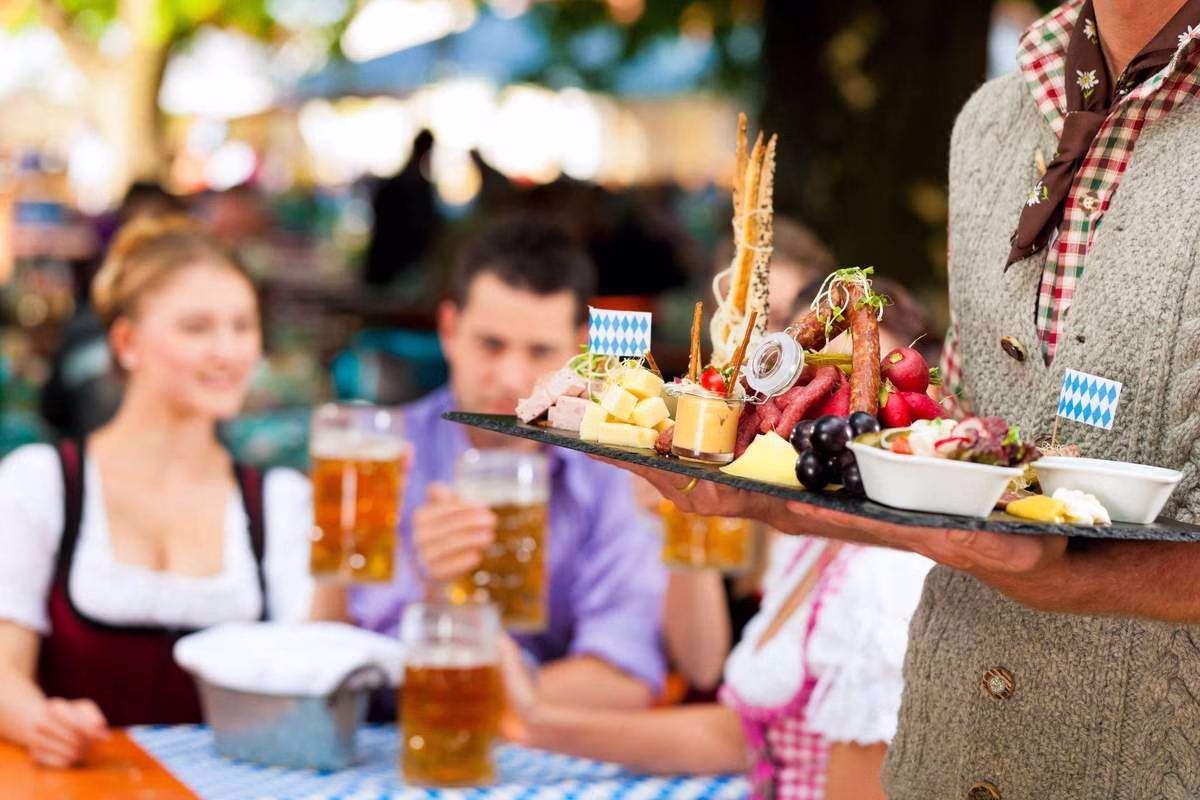 Bedienung mit Maßkrügen und Brotzeit im Biergarten